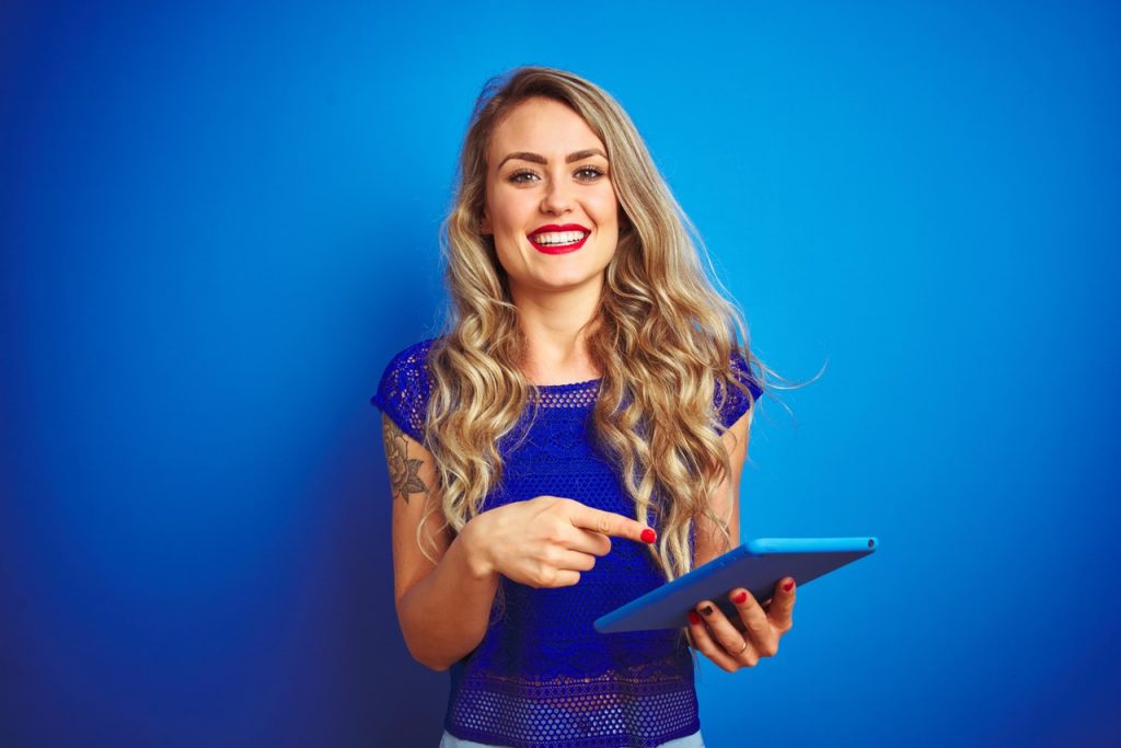 Girl dressed in blue on a blue background pointing to her tablet